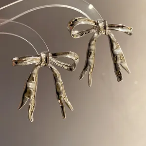 Macro detail of glossy silver liquid metal bow ribbon stud earrings for women.