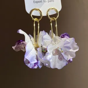 Close-up detail view of elegant fabric flower earrings with purple and white petals