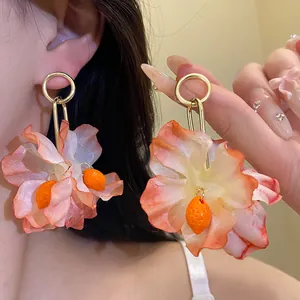 Detail view of large fabric flower earrings with orange fruit charms and gold hoops.