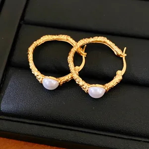 Macro close-up detail of textured golden hoop earrings featuring elegant white pearls