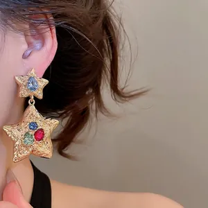 Chic gold-tone wrinkled star dangle earrings with multicolored rhinestones on a model