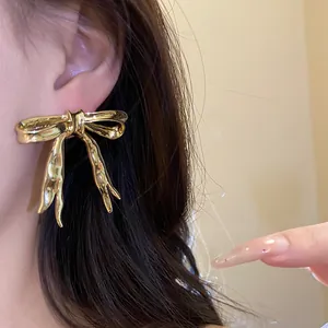 Detail view showing a golden vintage ribbon bow stud earring on a female model's ear