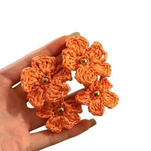 Beautiful handmade bohemian style orange woven flower stud earrings shown held in hand