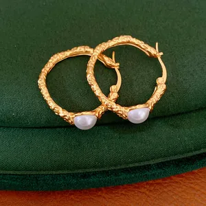 Close-up of golden textured hoop earrings with inset white pearl details