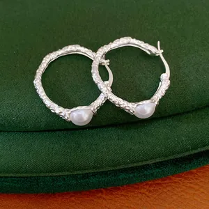 Detailed close-up view of silver textured hoop earrings featuring elegant white pearls