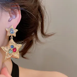 Close-up detail of luxury pleated gold star dangle earrings with colorful crystal accents