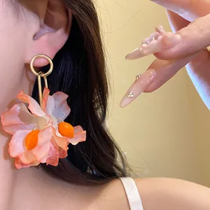 Detailed view of oversized orange fabric flower earring with gold-tone hardware on model.