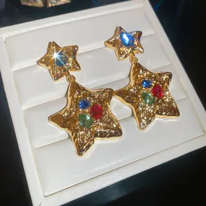 Gold hammered star earrings with multicolor crystals in luxury jewelry box display.