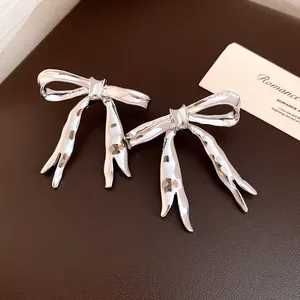 Close-up of silver-tone bow earrings with hammered texture on a brown surface