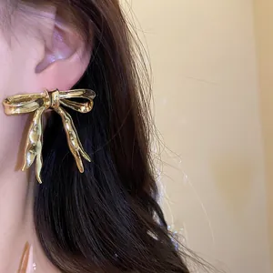 Close-up of golden metallic bowknot drop earring showing smooth polished finish and vintage style