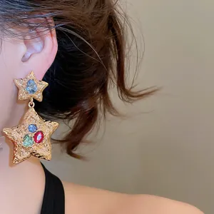 Detailed view of gold wrinkled star earrings with colorful rhinestones on a model