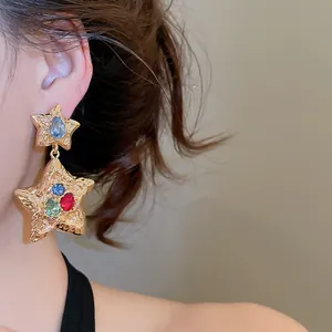 Detailed close-up of gold wrinkled star earrings featuring colorful crystal inlays on model