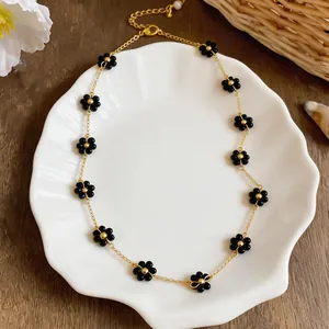 Close-up of a minimalist gold chain necklace with black beaded flowers on a shell plate.