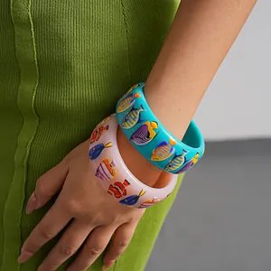 Nahaufnahme von farbenfrohen Fischprint-Armbändern aus Harz am Handgelenk eines Models