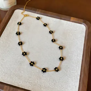 Detail view of black beaded flower necklace with gold chain on textured display board.