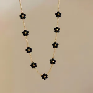 Macro view of a minimalist gold chain necklace featuring small black beaded flowers