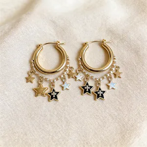 Close-up macro detail of gold hoop earrings with black enamel star charms and delicate chains