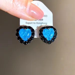 Detail of heart-shaped silver stud earrings with blue and black cubic zirconia stones.