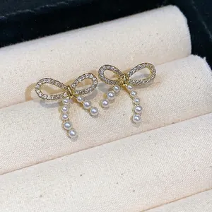 14k gold plated bow stud earrings with pearls and crystals on beige jewelry tray