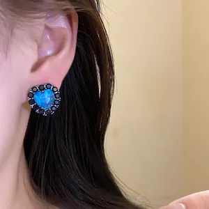 Close-up of elegant heart earring with blue stone and black zircons on model's ear