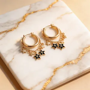 Close-up of gold star hoop earrings with black enamel charms and delicate chains