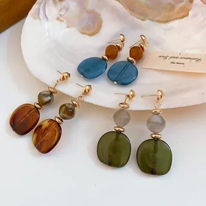 Detalle de pendientes geométricos de resina veteada en varios colores sobre bandeja de concha