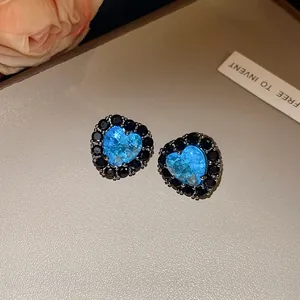 Detailed shot of heart-shaped stud earrings featuring a blue zircon and black halo