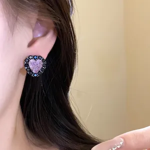 Close-up detail of a heart-shaped zircon stud earring with black stone trim worn on ear.
