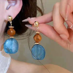 Primer plano de pendientes irregulares de resina azul con textura jaspeada y cuentas ámbar.