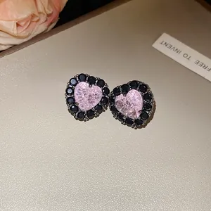 Macro view of pink heart-shaped zircon earrings with black stone halo on beige texture.