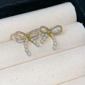 Detail view of dainty gold bow knot earrings with elegant hanging pearl tassels