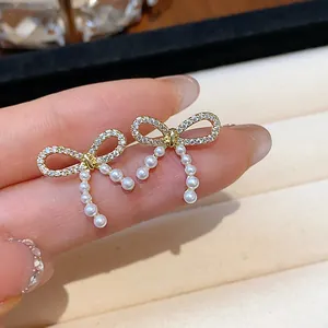Close-up of elegant bow stud earrings with sparkling crystals and pearl tassels.