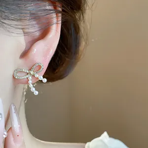 Close-up of 14k gold plated bow earrings with dangling pearls worn on ear.