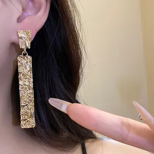 Macro detail shot showing gold-plated wrinkled rectangular drop earrings on model ear