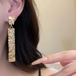 Detail shot of elegant golden rectangular earrings with unique crumpled texture on a model