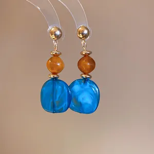 Vista detallada de pendientes de resina jaspeada azul con cuentas de ámbar y oro
