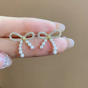 Close-up detail of 14k gold plated bow stud earrings with white pearls and sparkling crystals