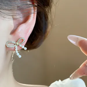 Close-up of gold-plated bow stud earring with sparkling stones and delicate pearls