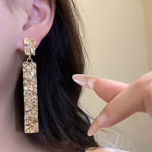 Detailed close-up view of gold wrinkled rectangular earrings with hammered texture.