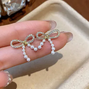 Close-up view of gold-plated bow earrings with micro-pave zircons and dangling pearls