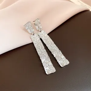 Detail view of minimalist silver rectangular earrings with a unique crumpled texture finish.