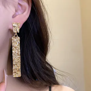 Macro detail of elegant gold rectangular drop earrings featuring a unique pleated texture