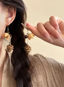 Close-up of vintage ethnic style earrings with flower and pinecone pendants on model.