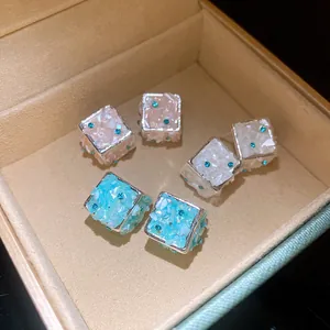 Dettaglio ravvicinato di orecchini a forma di cubo con trama in conchiglia e strass blu