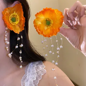 Close-up detail view of vibrant orange flower earrings with long pearl tassel drops