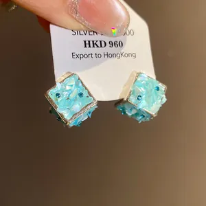 Dettaglio di orecchini a lobo quadrati in conchiglia azzurra con piccoli strass blu brillanti
