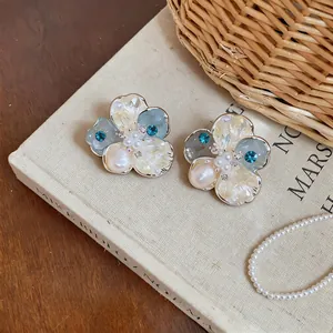 Detailed shot of flower-shaped stud earrings with blue zirconia and pearls on a book