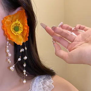 Elegant side view of large orange flower earrings with long pearl beaded tassels