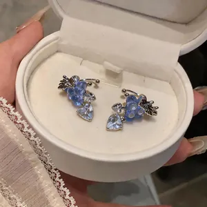 Close-up of elegant blue grape and heart zircon ear clips inside a white jewelry box