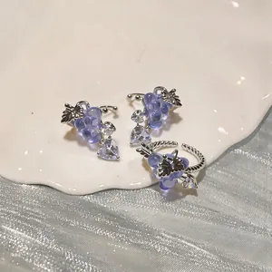 Detailed view of silver-toned grape ear clips and ring set with purple crystal stones